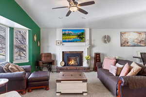 Carpeted living room featuring a brick fireplace, lofted ceiling, and ceiling fan