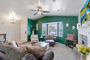 Carpeted living room featuring vaulted ceiling, a textured ceiling, and ceiling fan with notable chandelier