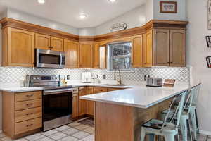 Kitchen with tasteful backsplash, vaulted ceiling, kitchen peninsula, sink, and appliances with stainless steel finishes