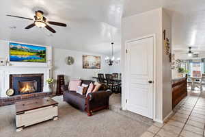 Living room with a textured ceiling, a fireplace, light tile patterned floors, and ceiling fan with notable chandelier