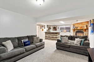 Living room with a textured ceiling, a stone fireplace, and carpet flooring