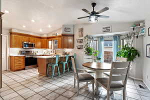 Tiled dining room featuring lofted ceiling, ceiling fan, sink, and a textured ceiling