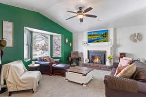 Carpeted living room featuring a brick fireplace, lofted ceiling, and ceiling fan