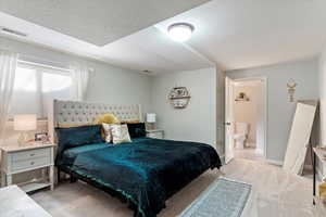 Carpeted bedroom featuring ensuite bath and a textured ceiling