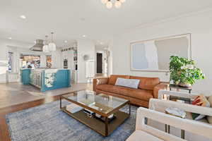 Living room with dark wood-type flooring, ornamental molding, and a notable chandelier