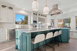 Kitchen featuring decorative light fixtures, white cabinetry, island exhaust hood, built in appliances, and a center island with sink