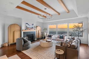 Living room with beam ceiling, a healthy amount of sunlight, a fireplace, and dark wood-type flooring