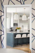 Kitchen with a kitchen breakfast bar, white cabinetry, built in appliances, and hanging light fixtures