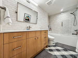 Full bathroom with toilet, vanity, tiled shower / bath combo, and tasteful backsplash