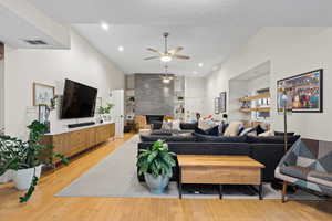 Living room featuring ceiling fan, a fireplace, a textured ceiling, and light wood-type flooring