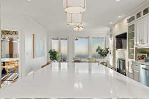 Kitchen with white cabinetry, a fireplace, hanging light fixtures, ornamental molding, and stainless steel dishwasher