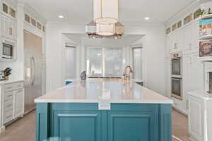 Kitchen with decorative light fixtures, white cabinetry, built in appliances, ornamental molding, and a large island