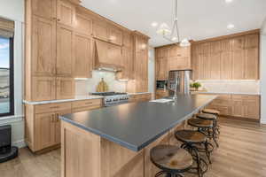 Kitchen with light hardwood / wood-style floors, appliances with stainless steel finishes, a center island with sink, and custom exhaust hood