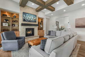 Living room with built in shelves, wood-type flooring, beamed ceiling, and a stone fireplace