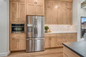 Kitchen with stainless steel appliances, light brown cabinetry, light hardwood / wood-style flooring, and tasteful backsplash