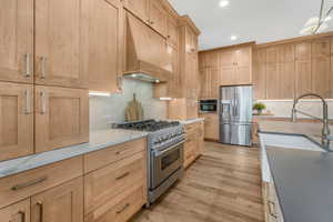 Kitchen featuring custom exhaust hood, sink, light hardwood / wood-style flooring, stainless steel appliances, and light stone counters