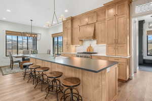 Kitchen featuring an island with sink, premium range hood, hanging light fixtures, sink, and stove