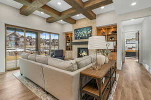 Living room with a fireplace, beam ceiling, coffered ceiling, light hardwood / wood-style flooring, and built in features