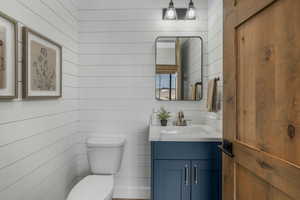 Bathroom with toilet, vanity, and wood walls