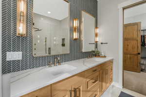 Bathroom featuring a shower with shower door, vanity, and tasteful backsplash