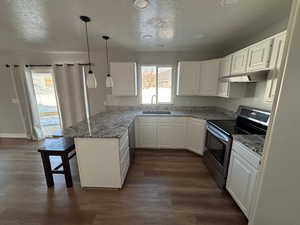 Kitchen with white cabinetry, a kitchen bar, kitchen peninsula, electric range, and sink