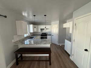 Kitchen with kitchen peninsula, hanging light fixtures, stainless steel range with electric cooktop, white cabinets, and dark hardwood / wood-style flooring