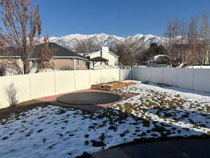 Yard layered in snow featuring a trampoline and a mountain view