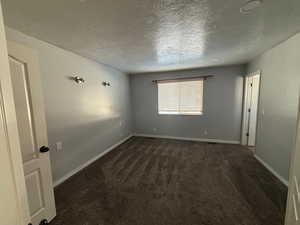 Spare room featuring dark carpet and a textured ceiling