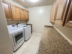 Washroom with cabinets, a textured ceiling, washer and clothes dryer, and light tile patterned flooring