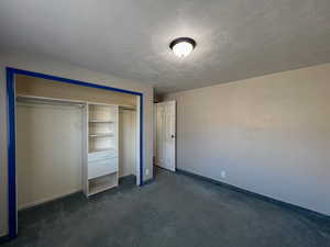 Unfurnished bedroom with dark carpet, a closet, and a textured ceiling