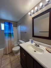 Full bathroom featuring shower / bathtub combination with curtain, vanity, a textured ceiling, tile patterned floors, and toilet