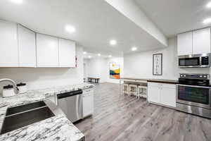 Kitchen with light hardwood / wood-style floors, sink, stainless steel appliances, and white cabinetry