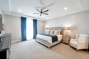 Bedroom with light carpet, ceiling fan, and a tray ceiling