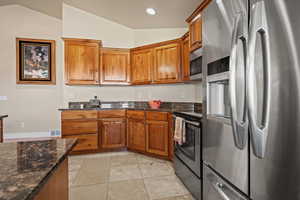 Kitchen featuring vaulted ceiling, light tile patterned floors, stainless steel appliances, and dark stone counters