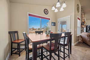 Dining area featuring vaulted ceiling, an inviting chandelier, light tile patterned floors, and a stone fireplace