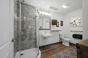 Bathroom with a textured ceiling, sink, toilet, walk in shower, and hardwood / wood-style flooring