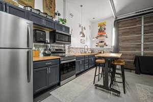 Kitchen featuring appliances with stainless steel finishes, butcher block counters, sink, backsplash, and hanging light fixtures