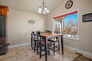 Tiled dining space featuring vaulted ceiling and a chandelier