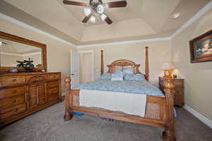 Carpeted bedroom featuring ceiling fan, a tray ceiling, and crown molding