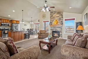 Living room featuring ceiling fan with notable chandelier, carpet, lofted ceiling, and a fireplace