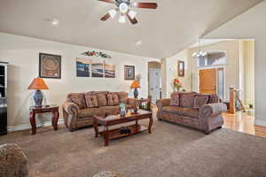 Carpeted living room with lofted ceiling and ceiling fan with notable chandelier