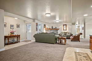 Living room featuring a textured ceiling, light carpet, and a stone fireplace