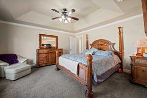 Carpeted bedroom featuring ceiling fan, a tray ceiling, and crown molding