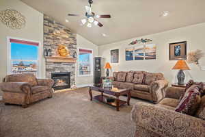 Living room with ceiling fan, high vaulted ceiling, a stone fireplace, and carpet flooring