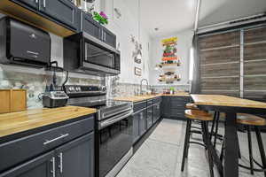 Kitchen with tasteful backsplash, pendant lighting, sink, appliances with stainless steel finishes, and butcher block counters