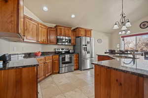 Kitchen with vaulted ceiling, pendant lighting, sink, appliances with stainless steel finishes, and a chandelier