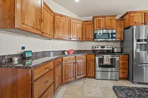 Kitchen with light tile patterned floors, appliances with stainless steel finishes, lofted ceiling, and dark stone countertops