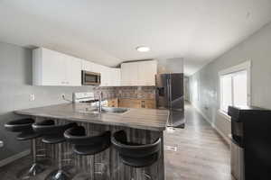 Kitchen featuring white cabinetry, a kitchen bar, kitchen peninsula, stainless steel appliances, and sink