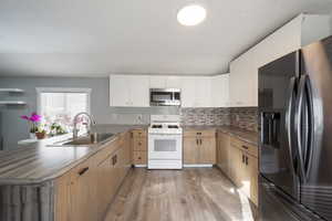 Kitchen featuring white gas range oven, light hardwood / wood-style floors, kitchen peninsula, black refrigerator with ice dispenser, and sink