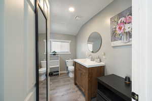 Bathroom with toilet, vanity, wood-type flooring, and lofted ceiling